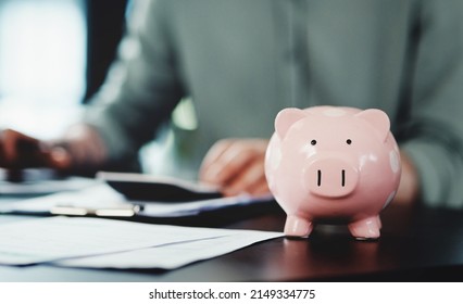 Saving Up For A Rainy Day With My Piggybank. Shot Of An Unrecognizable Businessman Doing Paperwork With A Piggybank On His Desk At Work.