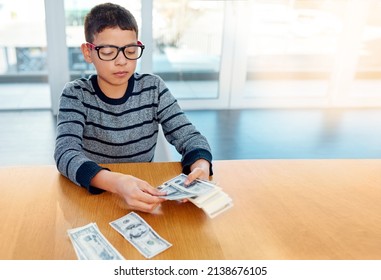 Saving Up For The Rainy Days. Shot Of A Focused Young Boy Counting His Money On The Dinner Table At Home.