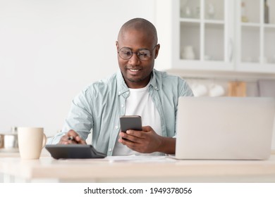 Savings And Finances Concept. Mature Black Man Using Calculator, Phone And Laptop Computer, Calculating Taxes, Sitting In Kitchen At Home, Copy Space