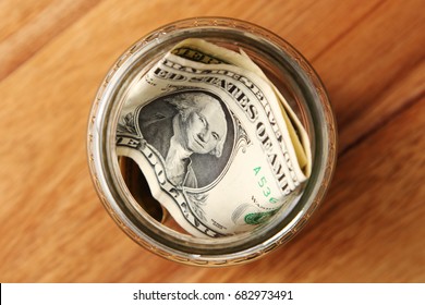 A savings jar filled with american dollars on a wooden table top.  