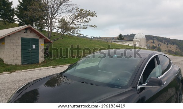 Savogna, Italy -\
May 04, 2020: Matajur Mountain, a static shot of a solid black\
Tesla Model 3 dual motor long range awd with tinted windows and\
aero wheels in a cloudy spring\
day
