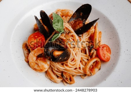 Savor a delicious seafood pasta with shrimp, mussels, squid, tomatoes, and basil on a white plate. Enjoy the delightful flavors and textures in this culinary experience.