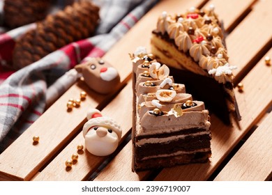 Savor festive joy with two decadent Christmas cakes on a wooden table, adorned with creamy layers, glistening gold balls, Santa and gazelle sugar, a cozy scarf, and pine cones.
