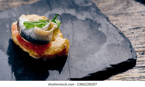 Savor the taste of gourmet sophistication with this exquisite canapé, featuring a silvery slice of anchovy elegantly perched atop a fresh bed of tomato on a crispy crostini.  - Powered by Shutterstock