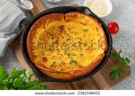 Savory cheese Dutch baby pancake. Dutch Baby pancake with mix tomatoes, parsley and arugula in cast iron pan on a concrete background. Delicious healthy breakfast