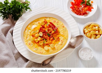 Savory Creamy Pumpkin Soup Topped With Fried Bacon, Shredded Cheddar Cheese And Salty Croutons In White Bowl On Wood Table With Ingredients