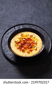 Savory Creamy Pumpkin Soup Topped With Fried Bacon, Shredded Cheddar Cheese And Salty Croutons In Black Bowl On Concrete Table, Vertical View