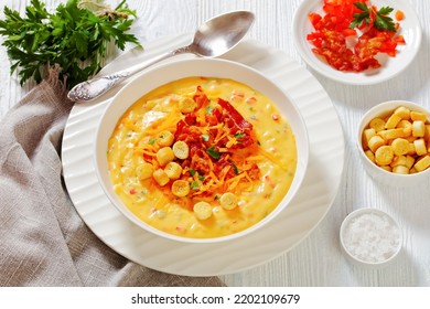 Savory Creamy Pumpkin Soup Topped With Fried Bacon, Shredded Cheddar Cheese And Salty Croutons In White Bowl On Wood Table With Ingredients