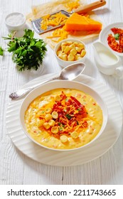 Savory Creamy Pumpkin Soup Topped With Fried Bacon, Shredded Cheddar Cheese And Salty Croutons In White Bowl On Wood Table With Spoon And  Ingredients,vertical View From Above