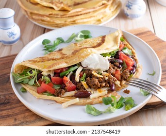 Savory Crepe Filled With Spicy Ground Beef, Cheese, Kidney Beans, Lettuce And Tomatoes. Topped With Sour Cream And Served On A Plate. Tex Mex Food