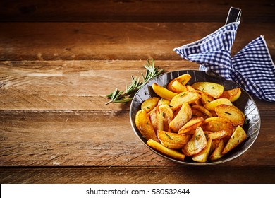 Savory Crispy Golden Roast Potato Wedges With Fresh Rosemary Served In An Old Vintage Skillet On Rustic Wooden Boards With A Checkered Blue And White Napkin And Copy Space