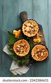 Savory hands pie with chanterelle mushrooms, cream and cheese on cutting board on rustic old wooden table background. Homemade tarts with seasonal chanterelle mushrooms. Rustic style. Top view.