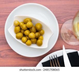 Savory pickled green olives served in white bowl with glass of light wine for relaxing dinner. Traditional Spanish appetizer - Powered by Shutterstock