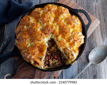 Savory pie with minced meat and cabbage. Topped with baked mash potato crust and cheddar cheese. Served in cast iron skillet on wooden table. Table top view