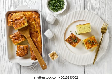 savory potato kugel, baked pudding or casserole of grated potato cut in portions in a baking dish and served on a white plate on a wooden table, jewish holiday recipe, flat lay, free space