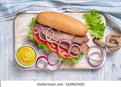 Savory Sandwiches Of Hoagie Bread Rolls With Beef And Vegetable: Tomatoes, Cheese, Red Onion, Lettuce Leaves, Served With Mustard And Barbeque Sauce, On A White Wooden Background, Close-up