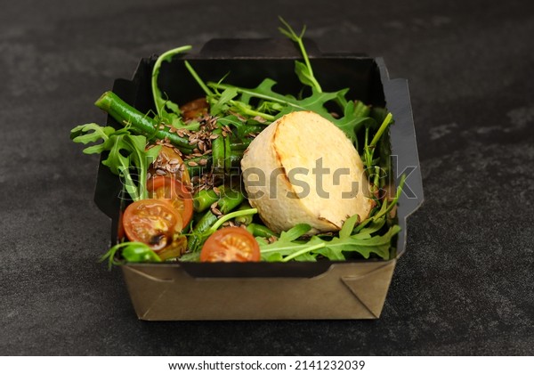 Savory souffle salmon and salad with arugula,
tomatoes and green beans in black paper takeaway box on dark
background. Healthy food delivery
concept.