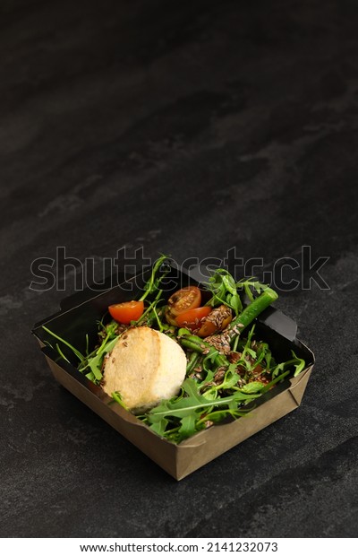 Savory souffle salmon and\
salad with arugula, tomatoes and green beans in black paper\
takeaway box on dark background. Healthy food delivery concept.\
Free space for text.
