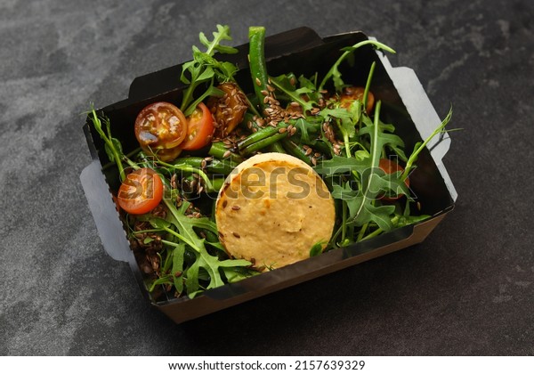 Savory souffle salmon and salad with arugula,
tomatoes and green beans in black paper takeaway box on dark
background. Healthy food delivery
concept.