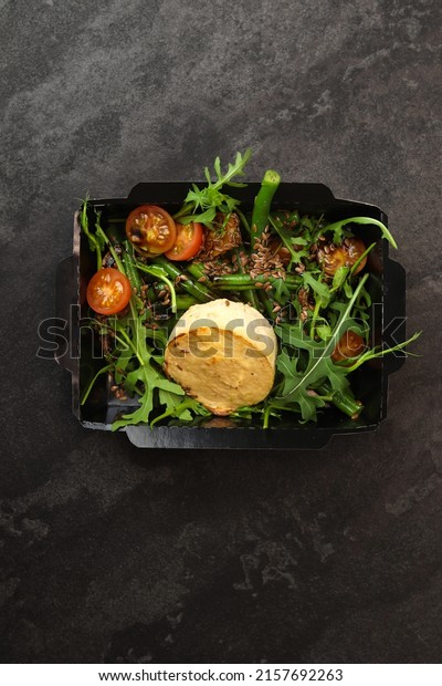 Savory souffle salmon and salad with arugula,\
tomatoes and green beans in black paper takeaway box on dark\
background. Healthy food delivery\
concept.