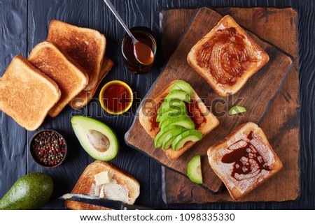 savory toasts for breakfast with butter, avocado slices and healthy food spread made from leftover brewers yeast extract with vegetables and spices, view from above, flat lay