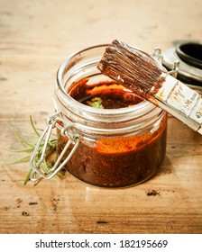 Savoury BBQ Basting Sauce In A Glass Jar With A Basting Brush And Sprig Of Fresh Rosemary For Seasoning And Flavoring The Meat