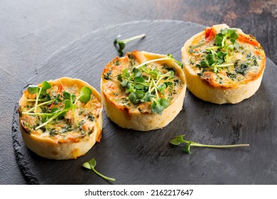 Savoury mini quiches with custard and watercress on a black round wooden board - Shutterstock ID 2162217647