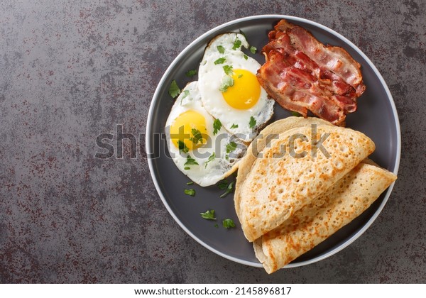 Savoury oat pancake perfect for breakfast with\
bacon and fried eggs close-up in a plate on the table. Horizontal\
top view from above\
