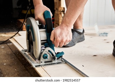 Sawing plywood by circular saw. Home repair. Hand tool. Man hold equipment. Building process. Woodworking. Safety engineering. Without gloves. Copy space. Indoor. Cutting material. Rental instrument.