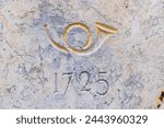 Löbau, Saxony - Germany - 04-17-2021: Close-up of a golden stone engraving depicting a post horn with the year 1725 in Löbau