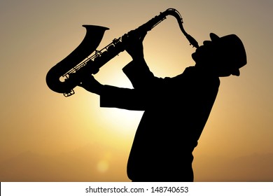 Saxophonist. Man playing on saxophone against the background of sunset 