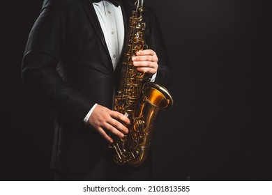 Saxophonist Plays Jazz. Male Musician in a Formal Black Suit Holds a Tenor Saxophone on a Dark Background. Saxophone Close-up. Copy space High quality photo - Shutterstock ID 2101813585