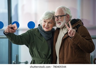 Say Chees. Waist Up Of Happy Gray-haired Man And Elegant Old Woman Are Standing Together And Smiling While Taking Selfie Using Modern Smartphone