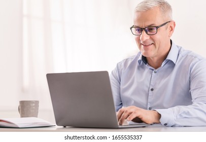 Say No To Ageism Concept. Happy Senior Man Working On Laptop Computer Sitting In Modern Office, Empty Space