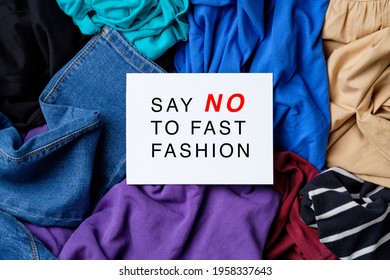 Say NO To Fast Fashion Sign On White Paper Over Heap Of Female Clothes