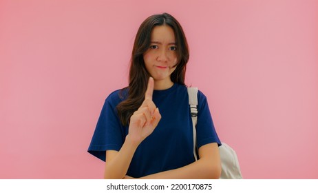 SAY NO, Serious Young Asian Woman Doing Warning Or Disapproving Sign, Don't Do It, I Don't Need It Or Not Allowed With Finger Shaking Admonishing Gesture Looking At Camera. Isolated On Pink Background