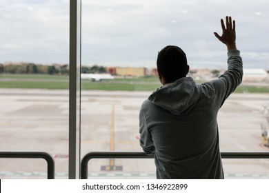 Saying Goodbye At The Airport. Young Man Traveler Waves His Hand To Departure Plane.