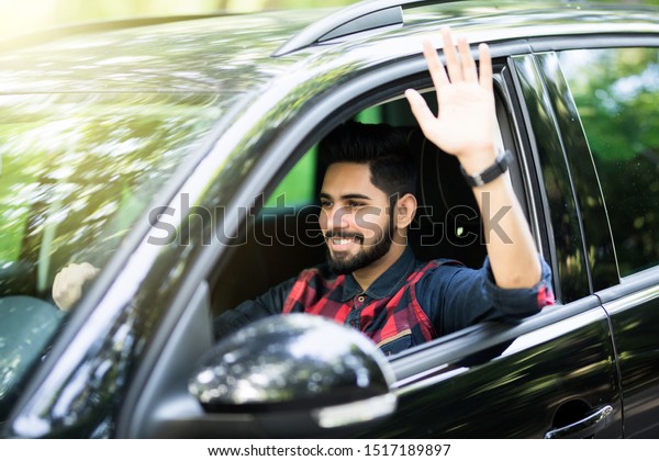 Saying hello. Handsome young\
smiling businessman sitting in new car and waving his to\
someone.