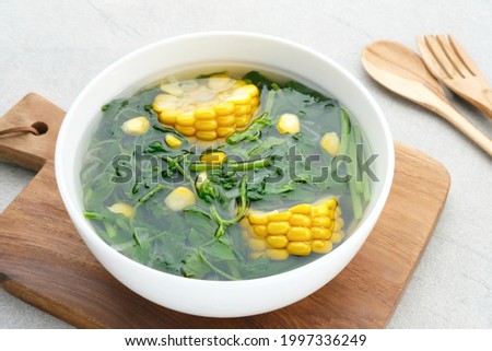 Sayur Bening Bayam, Spinach Clear Vegetable. Indonesian food of spinach, spinach soup with corn. Served in white bowl on grey background. Close up.
