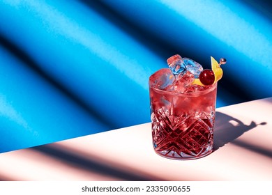 Sbagliato Rosa alcoholic cocktail drink with Italian red liqueur and aperitif, champagne rose or sparkling wine, decorated with zest, summer blue bright background, hard light and shadows