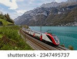 An SBB double deck train travels along the shore of beautiful Lake Walen (Walensee) with rugged alpine mountains (Churfirsten Mountain Range) in background, in Quarten village, St. Gallen, Switzerland
