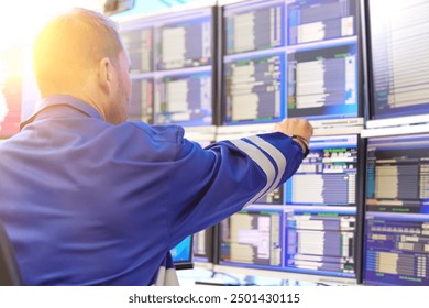 SCADA system in central heating process.  Operator wearing blue overall is Analyzing Data on Multiple Monitors - Ensuring Optimal Performance and Safety in Industrial Automation Systems.