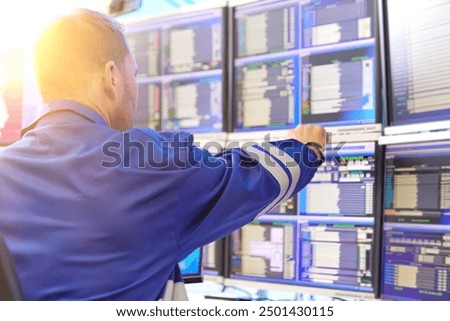 SCADA system in central heating process.  Operator wearing blue overall is Analyzing Data on Multiple Monitors - Ensuring Optimal Performance and Safety in Industrial Automation Systems.