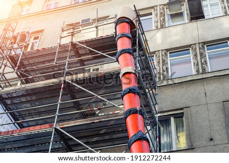 Scaffolding with big red plastic slide chute for rubble debris removal on old historica building facade renewal construction site in city street. Industrial development engineering equipment