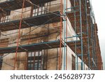 Scaffolding on a generic old tenement house, renovated historical building facade detail, closeup, nobody. Restoration industry, old architecture, real estate renovation simple concept