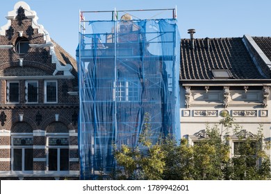 Scaffolding with protective net against historic building to prevent paint and building material from falling on the street and people, during renovation in a street in Maastricht, the Netherlands