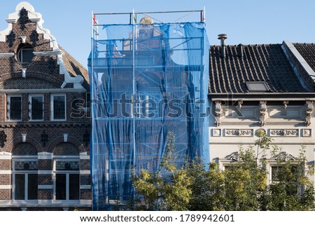 Scaffolding with protective net against historic building to prevent paint and building material from falling on the street and people, during renovation in a street in Maastricht, the Netherlands