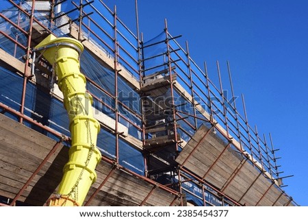 Scaffolding and scaffolding with yellow debris chute with a blue sky