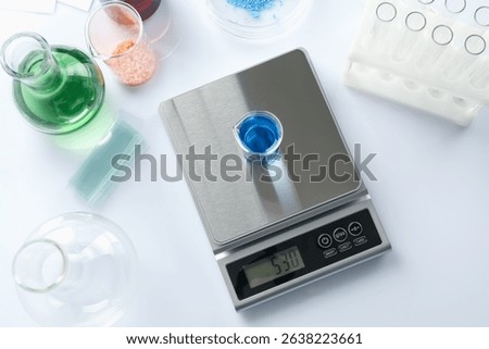Scale with beaker of sample and other laboratory equipment on white background, flat lay