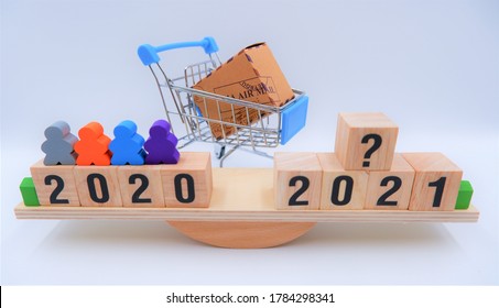 Scale Comparing 2020 And 2021 With Shopping Cart. Online Shopping Market Analysis Concept, Question On Future Consumer Volume And E-commerce Marketing Trends, Economic Impact From Coronavirus Crisis.